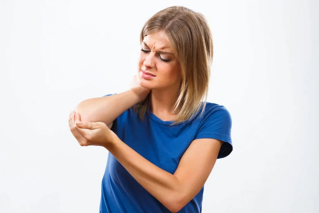Woman with shoulder-length blonde hair wearing a blue shirt, holding her elbow and showing discomfort.