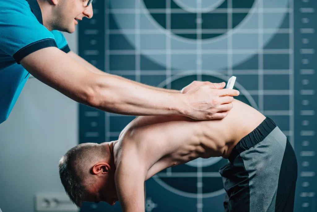 Chiropractor examining a patient's back during a scoliosis assessment in a clinical setting.
